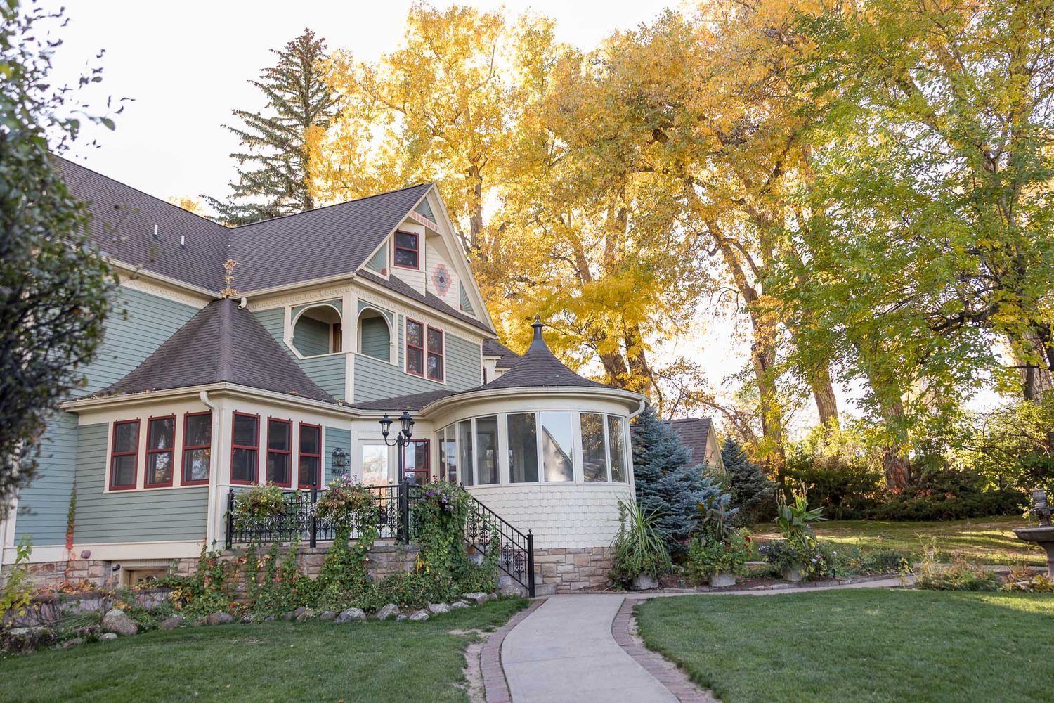 Beautiful Victorian-style home with wraparound porch and autumn trees glowing golden in late afternoon sunlight.