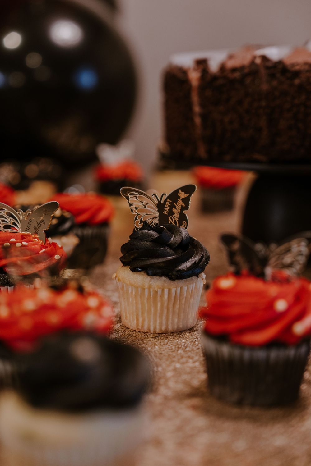 Black and red cupcakes decorated with delicate butterfly toppers on a sparkly surface.