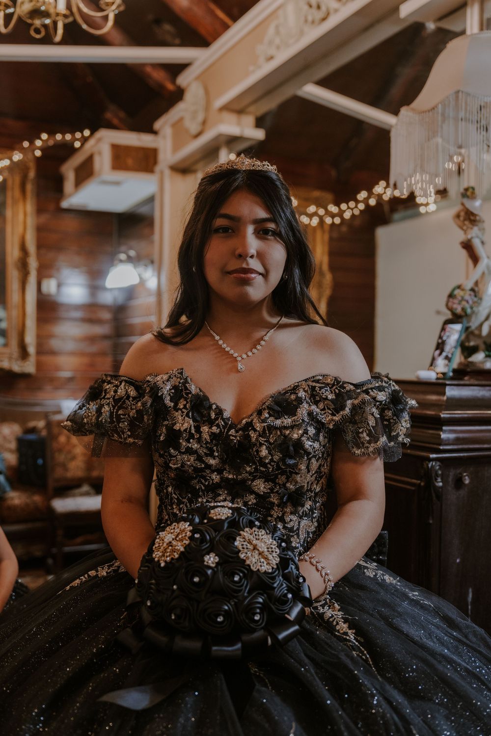 Elegant black ball gown with gold embroidery and off-shoulder design in a rustic venue.
