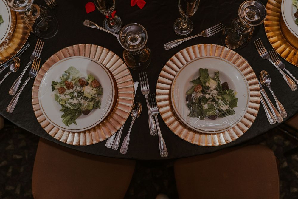 Two elegant place settings with striped plates and salads on a dark table with wine glasses and decorative lighting.