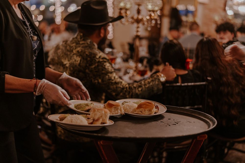 Server carrying plates of food in dimly lit restaurant with festive atmosphere.