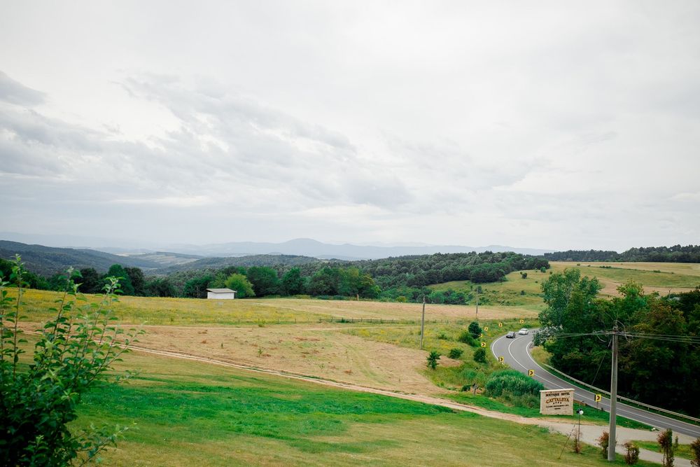 Panoramic view of rolling green hills and winding country roads through a rural landscape on a cloudy day.