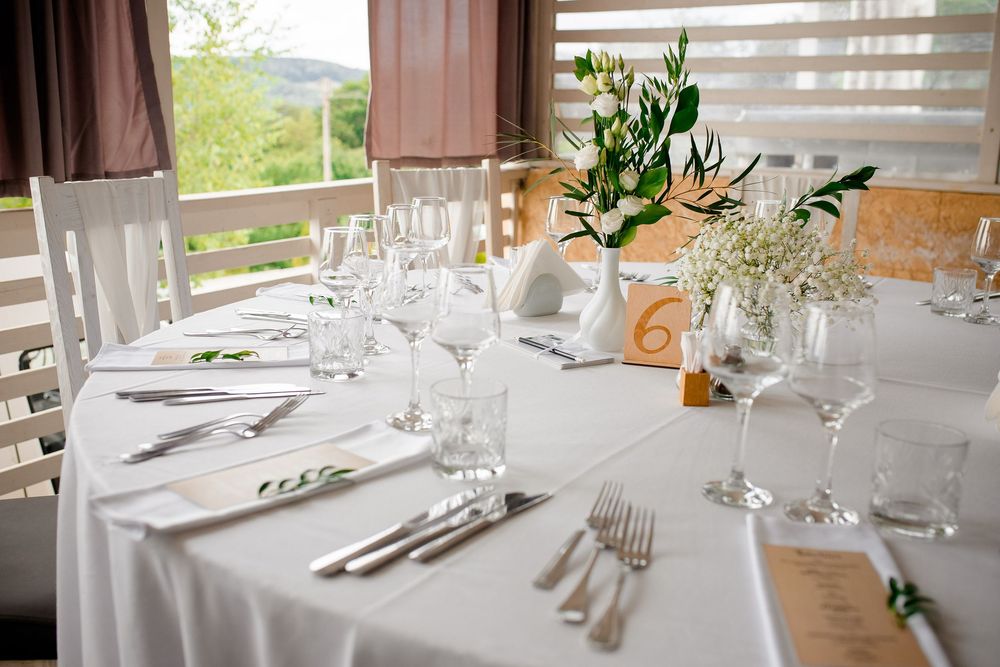 Elegant wedding reception tables set with white linens, floral centerpieces, and formal place settings in a rustic venue.