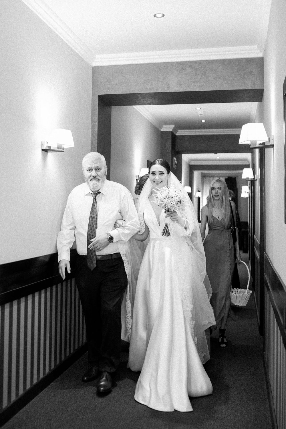 Wedding party walking down a bright hallway with the bride in a flowing white gown.