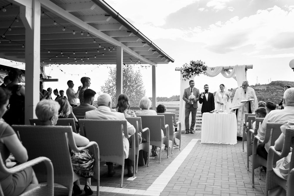 Panoramic view of people dining outdoors at a coastal restaurant with ocean views and covered seating area.