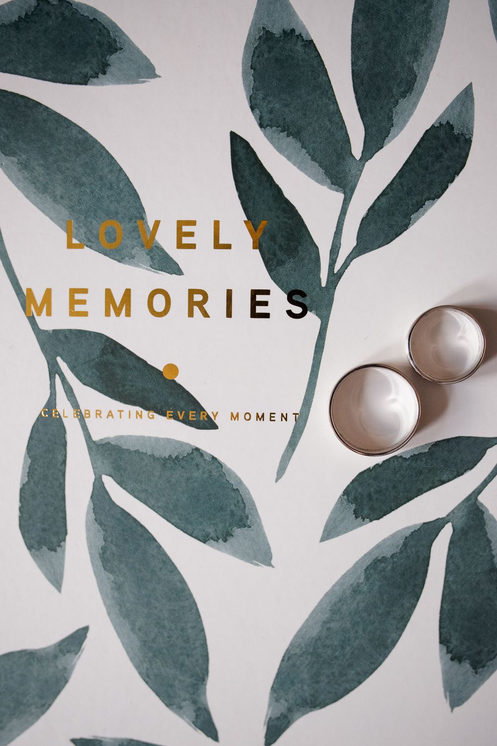 Elegant wedding album cover design with green watercolor leaves and gold text against white background.