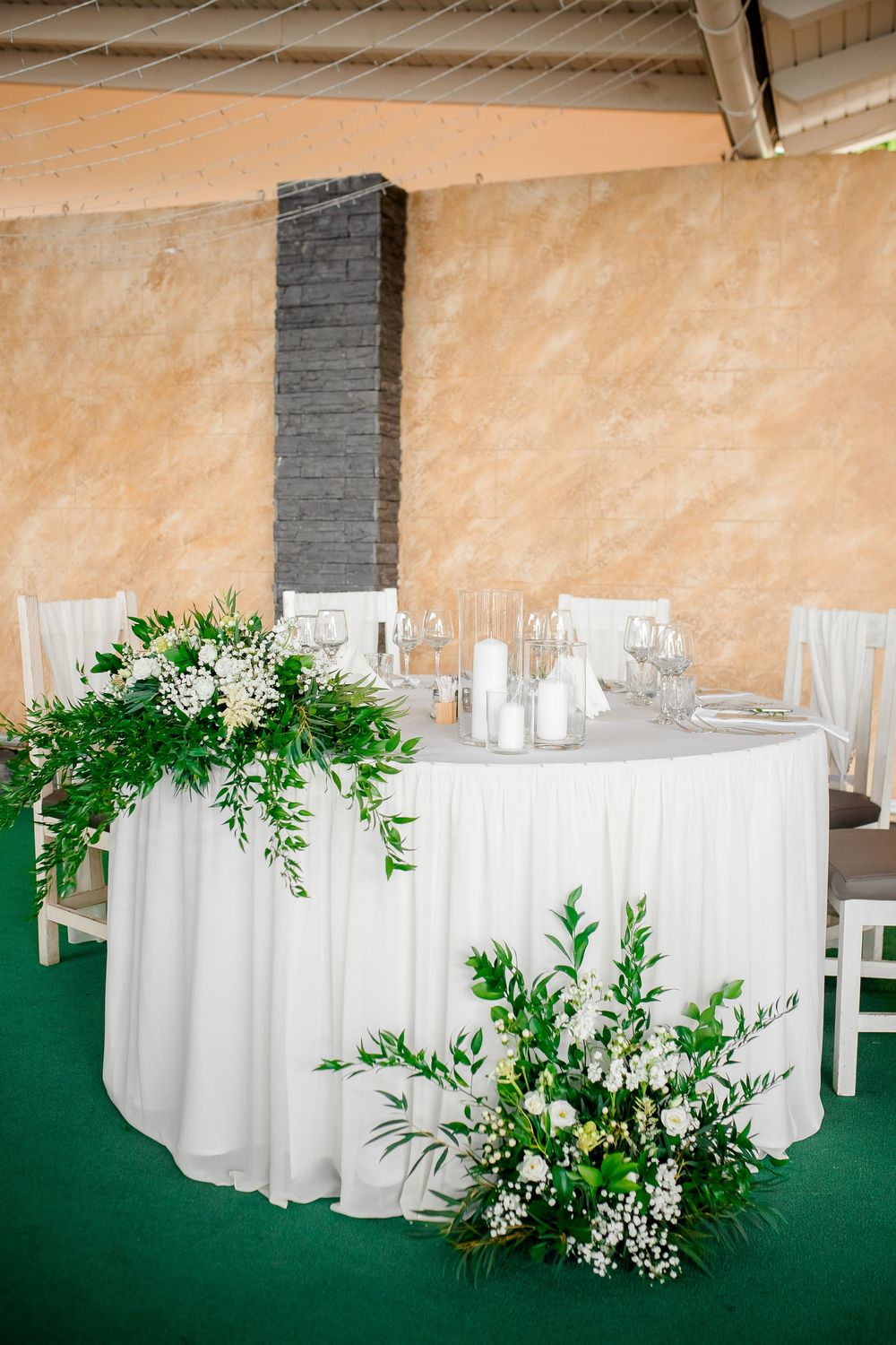 Elegant wedding reception tables with white linens and lush greenery decorations in an indoor venue.