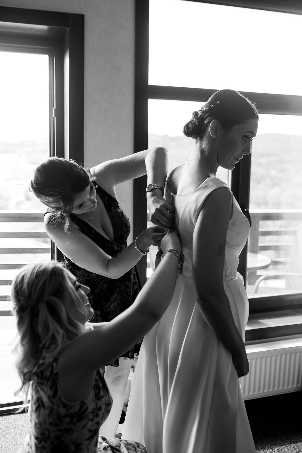 Black and white sequence showing a wedding dress being fitted and adjusted on a mannequin near a bright window.