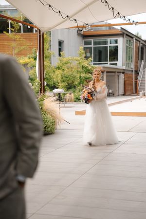 A wedding couple shares a romantic first look moment on a modern patio with glass walls and greenery in the background.