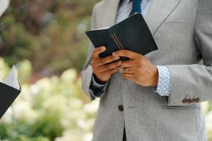 Professional in a gray suit holds a smartphone while standing against a blurred background.