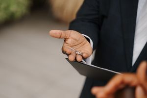 A person in a suit jacket adjusts their tie while standing outdoors.