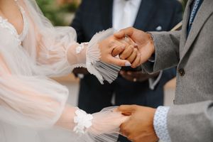 A close-up shot of hands during a ring exchange ceremony with delicate lace details visible.