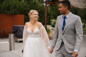 A couple shares a joyful moment together during their outdoor wedding celebration, with the bride in white and groom in gray.