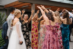 Wedding party celebrates with raised arms and joyful expressions during outdoor celebration in floral dresses.