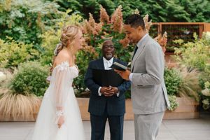 A wedding ceremony takes place in a lush garden setting with floral arrangements and natural greenery.