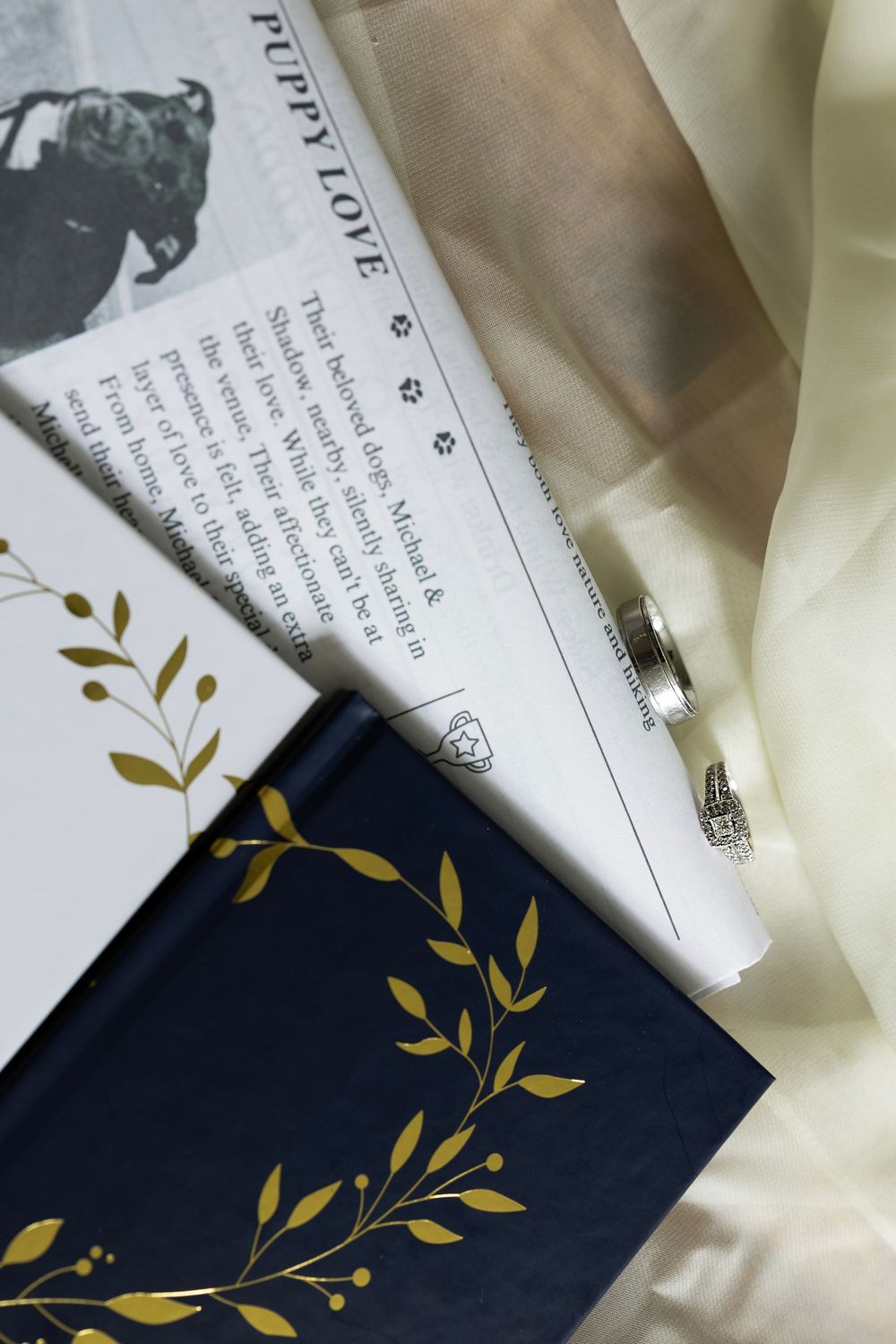 Artistic flatlay of navy blue wedding invitations with gold leaf botanical details against white fabric background.