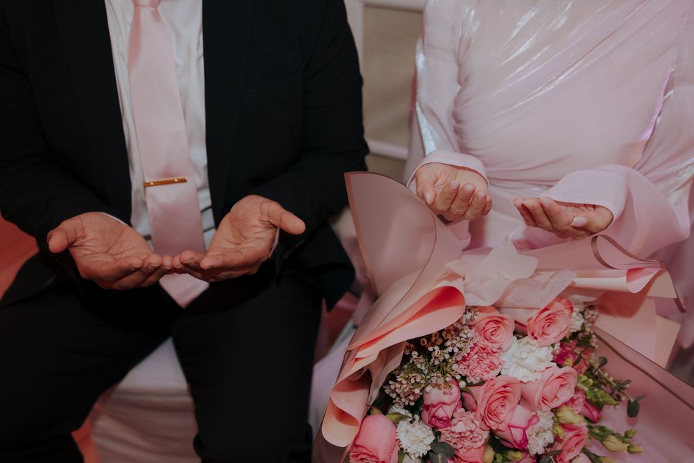 Hands hold beautiful pink and white roses in a wedding bouquet against a backdrop of formal attire.