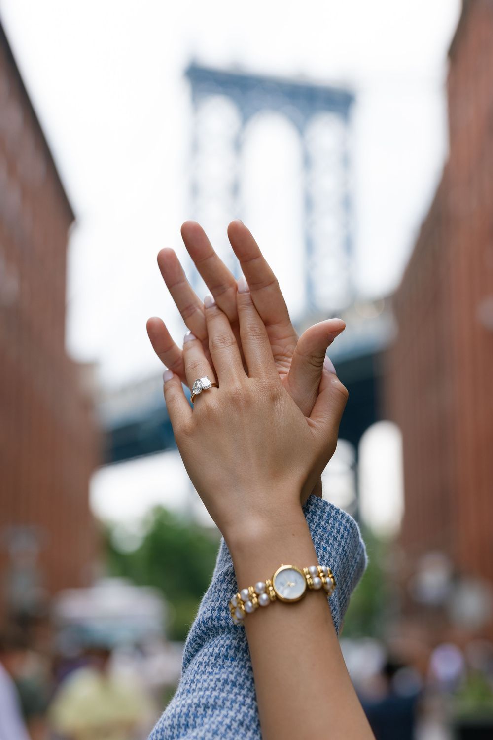 A series of hands raised in the air wearing rings and bracelets with the Manhattan Bridge visible in the background.