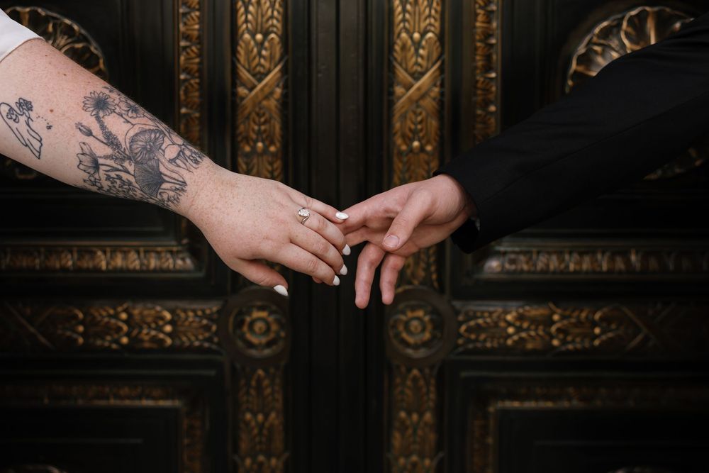 Two hands touching, one with tattoos and a ring, against an ornate golden door.