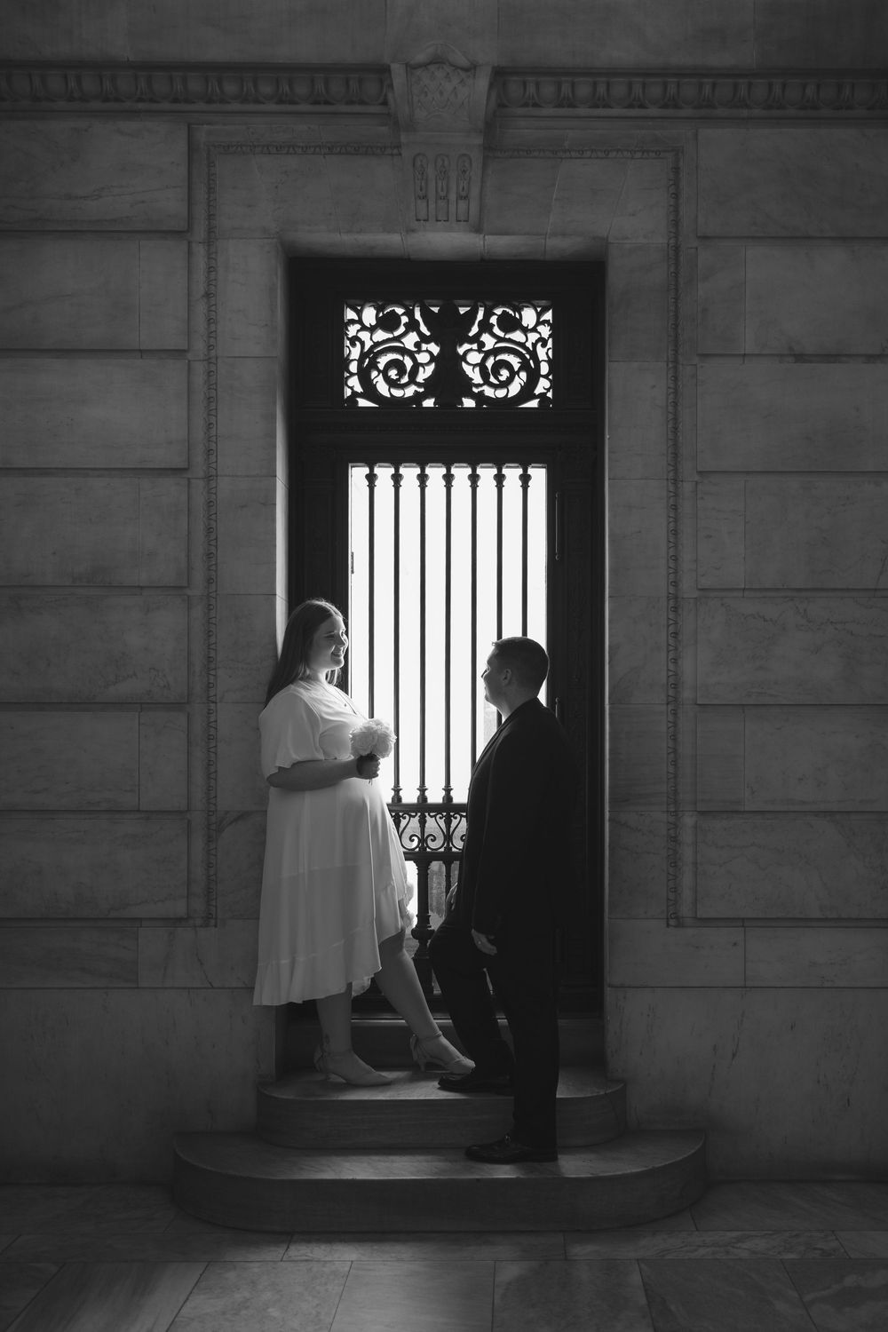 Black and white photo of a couple sharing a romantic moment in an ornate doorway on stone steps.