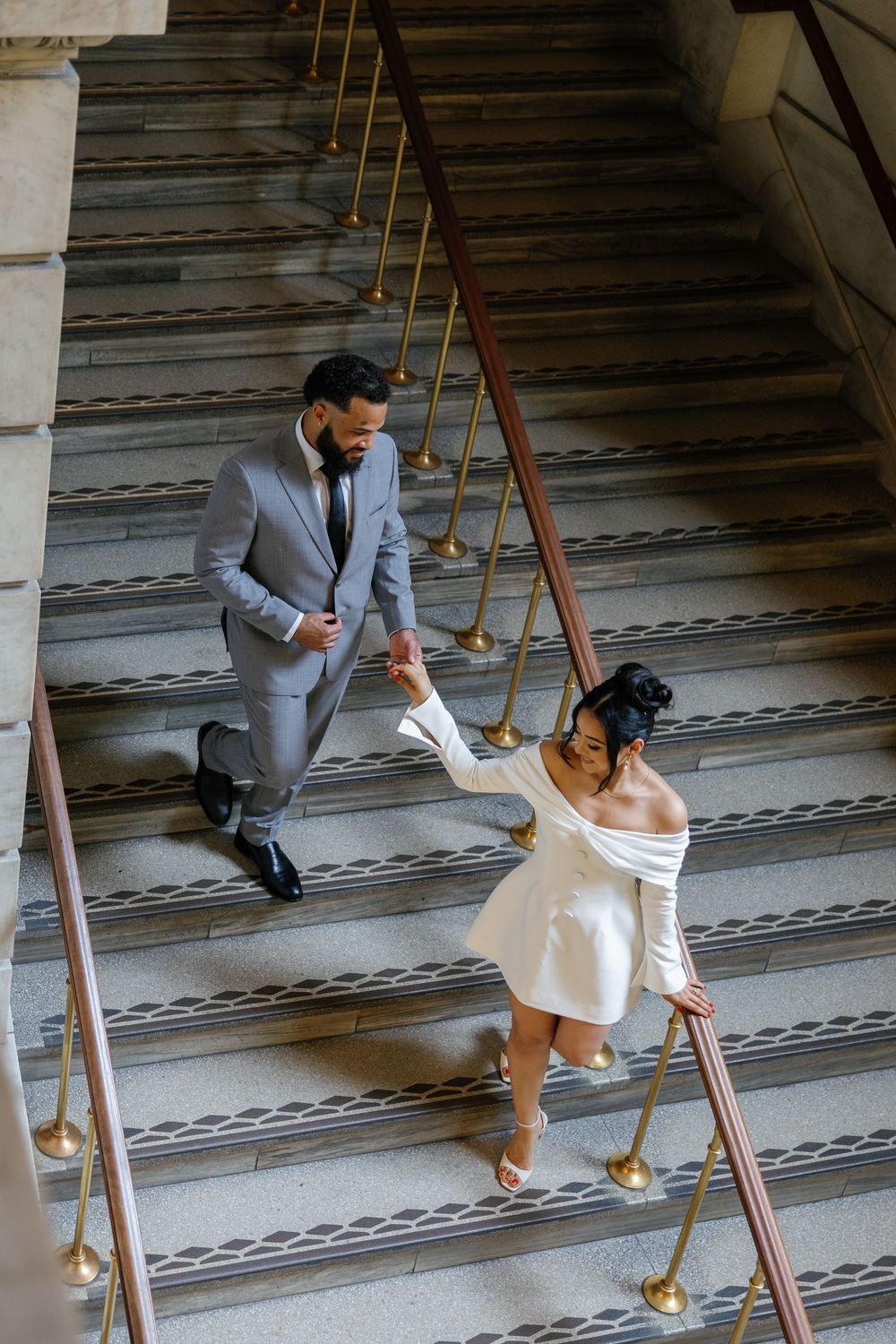 A couple in wedding attire playfully poses on a grand staircase in sequence showing movement and joy.