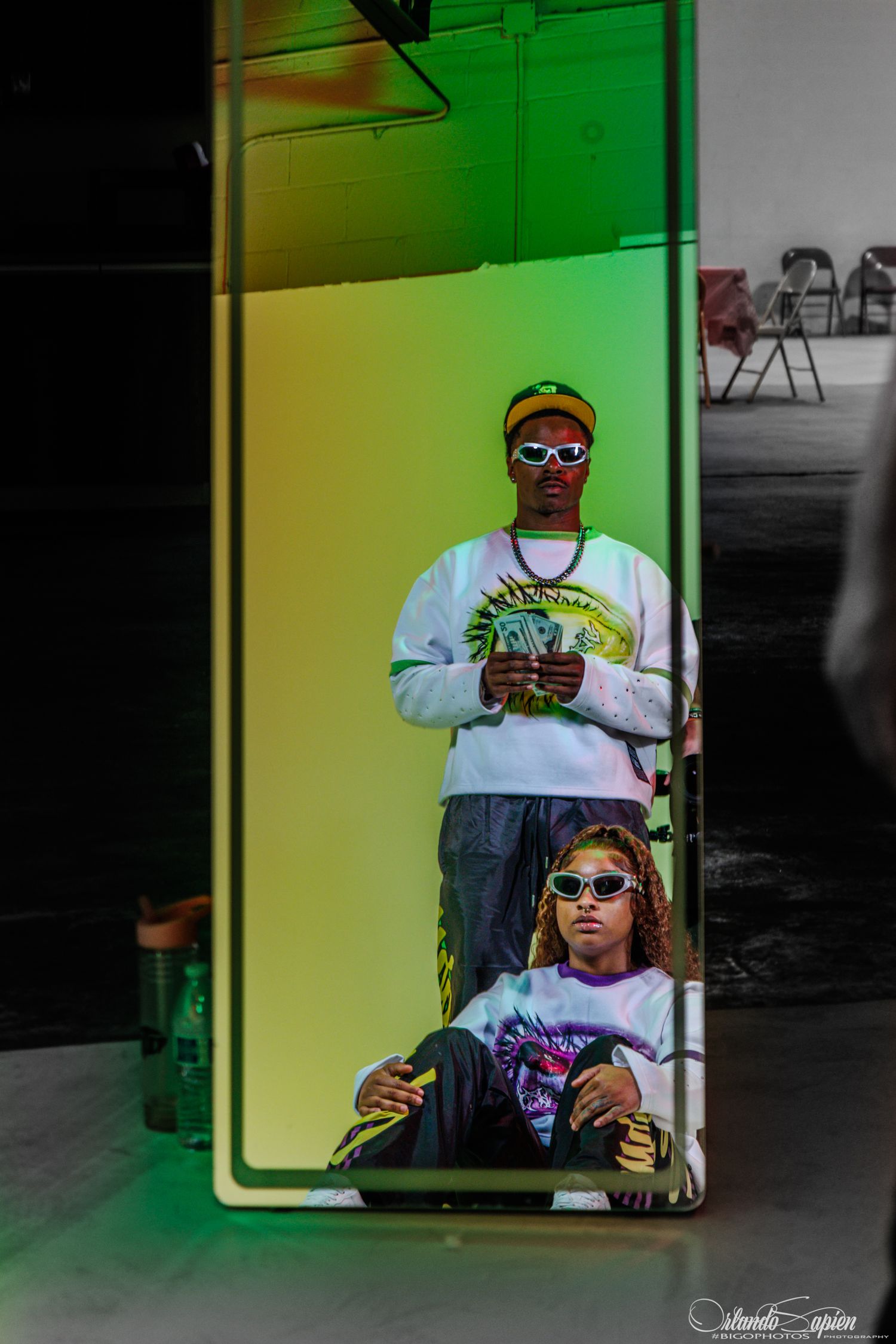 A person wearing sunglasses and a light colored shirt sits behind a window with a green glow in the background.