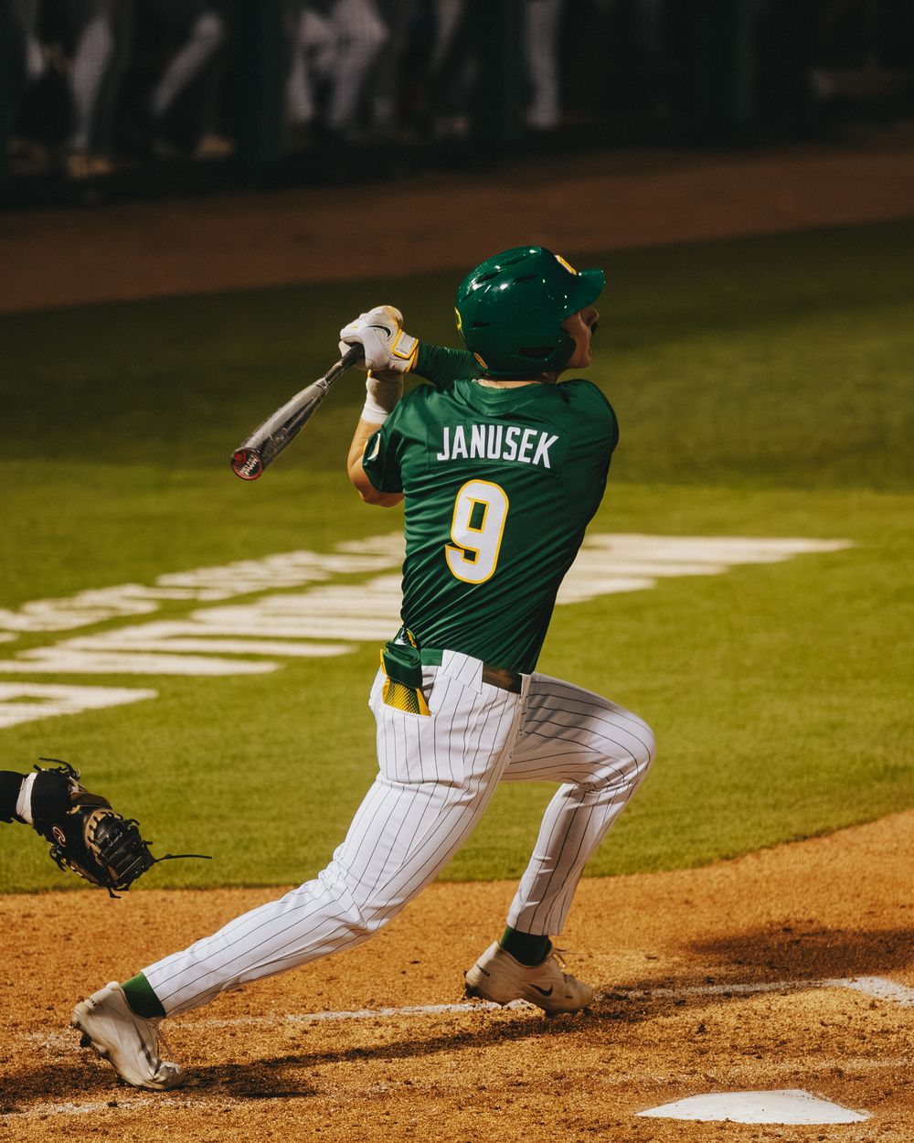 Baylor Bears baseball player Janusek number 9 swings the bat during a college baseball game at night.