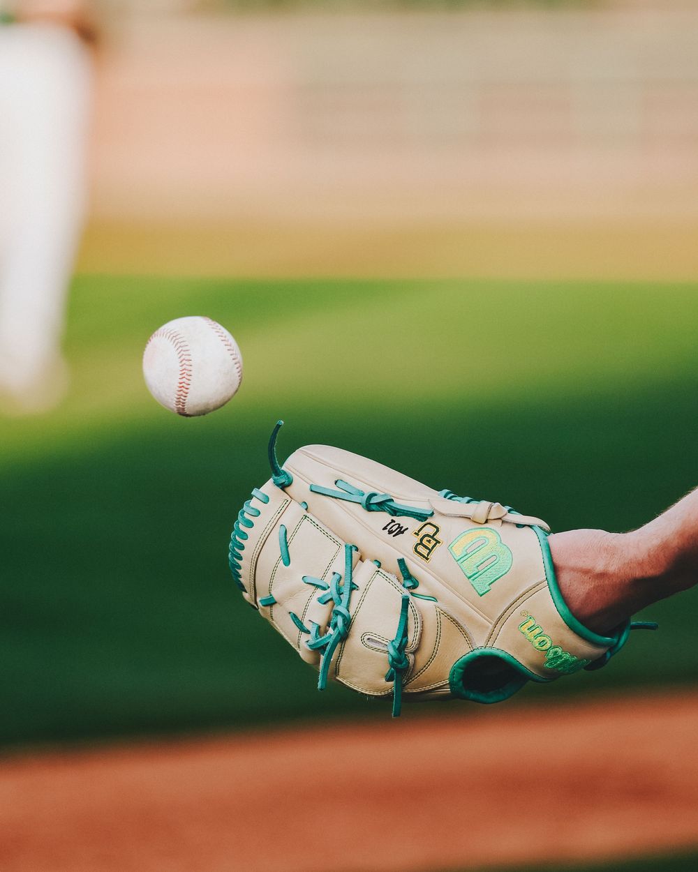 Close-up of a Wilson baseball glove with teal laces catching a baseball during a Baylor Bears game.