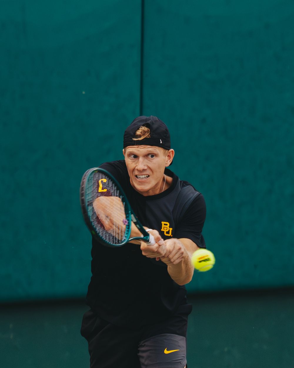 A focused Baylor University tennis player hits a backhand shot during a competitive match.