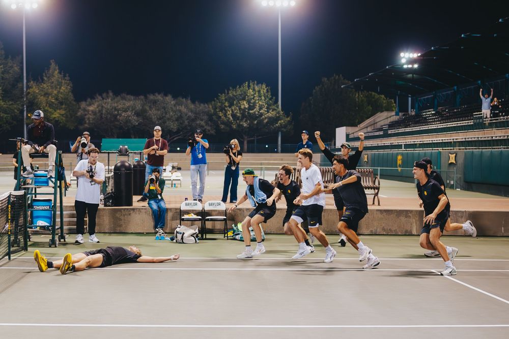 Baylor University tennis team celebrates a victory together on an outdoor court at night.