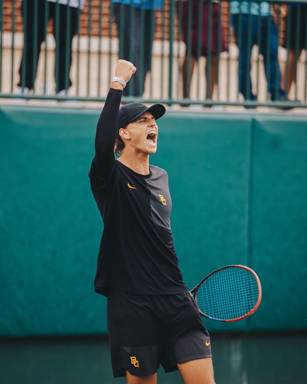 A tennis player in black Baylor University uniform celebrates victory with raised fist on court.