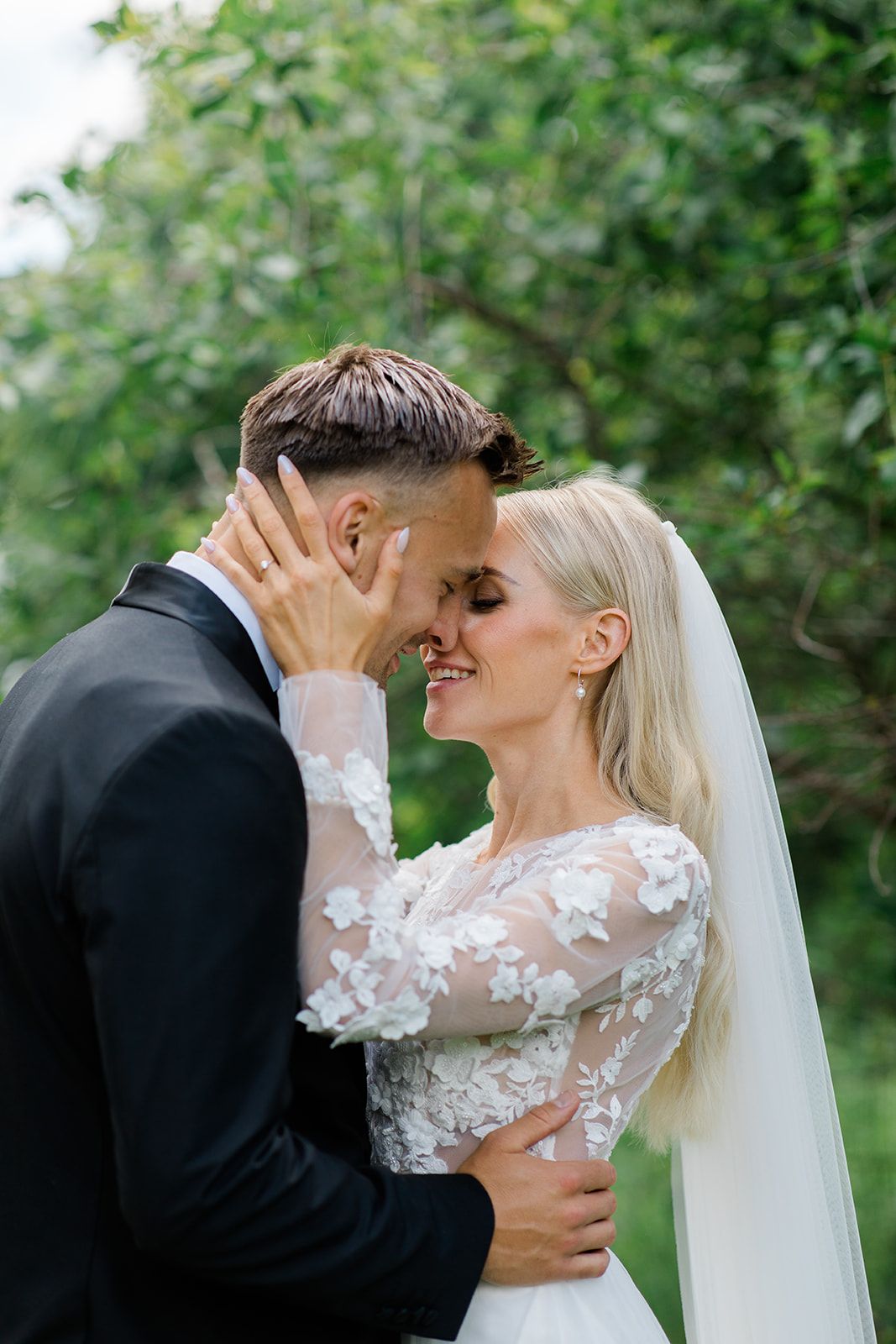 A romantic wedding couple shares an intimate moment outdoors surrounded by lush greenery.