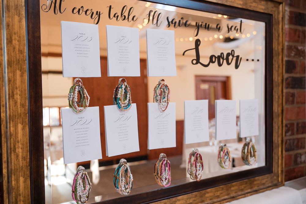 Wedding seating assignments displayed on white cards against a rustic wooden wall with string lights.