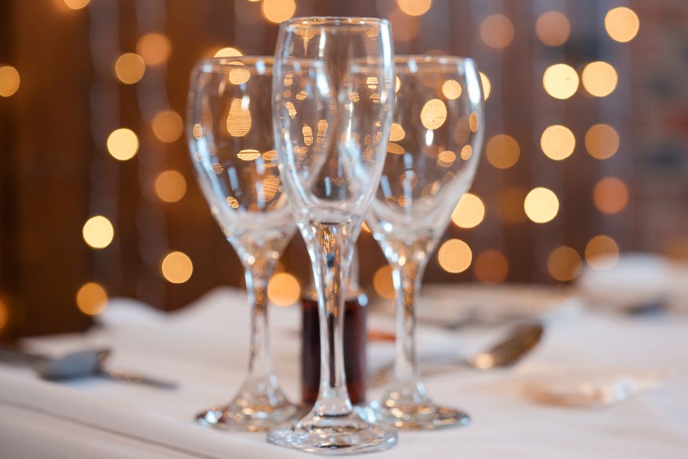 Close-up of wine glasses on a formal table setting with blurred bokeh lights in the background.