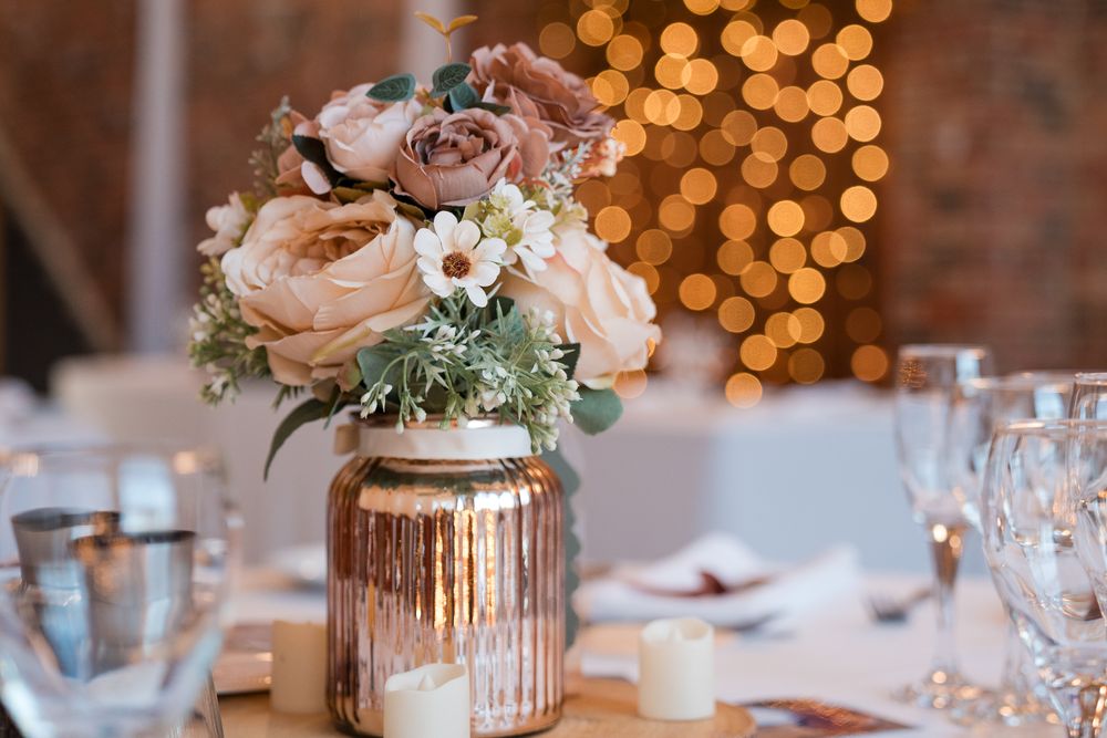 Elegant wedding reception table with soft pink roses in mercury glass vases and glowing bokeh lights in background.
