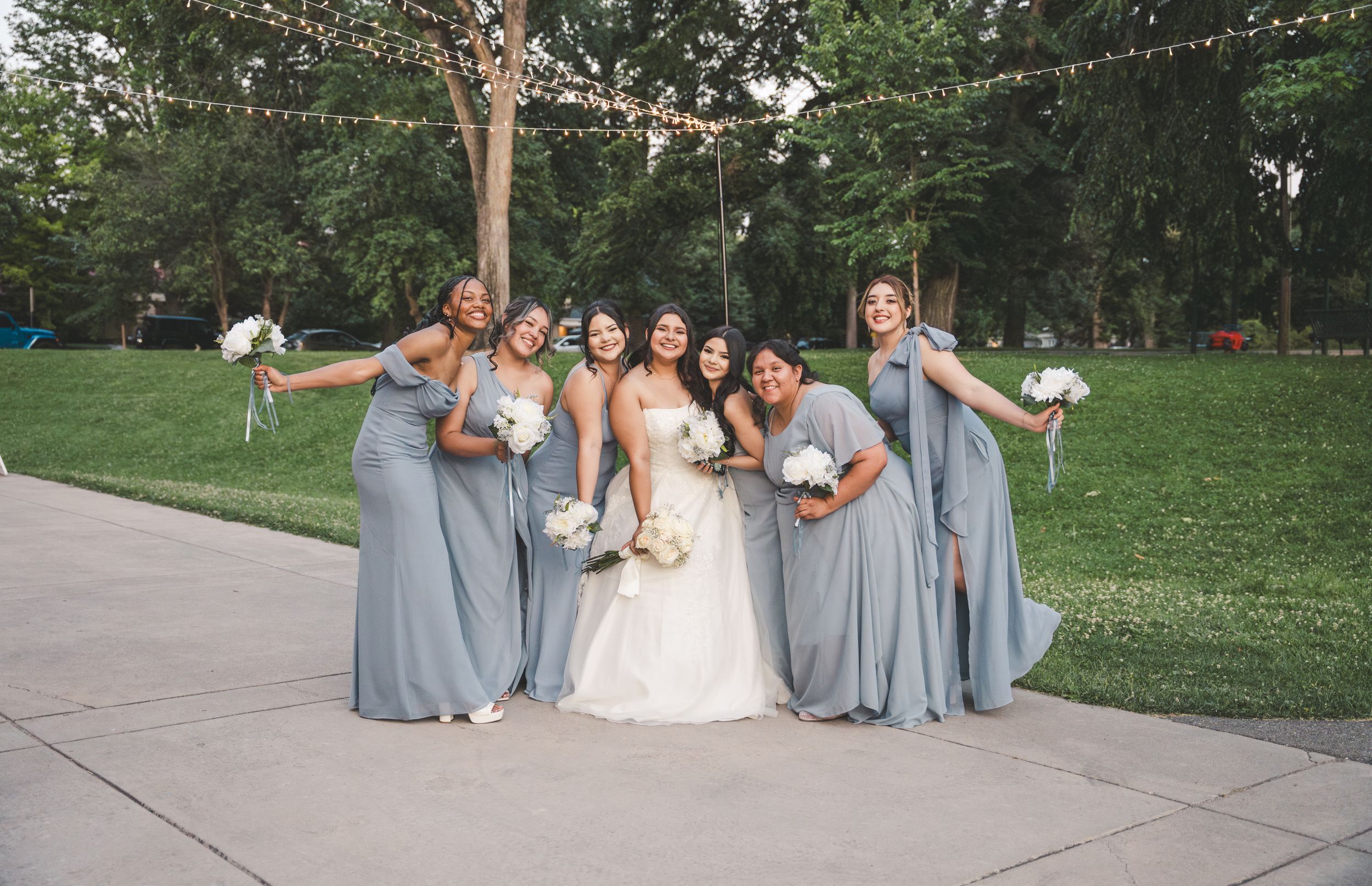 Wedding party in light blue bridesmaid dresses poses together on a grassy lawn during summer celebration.