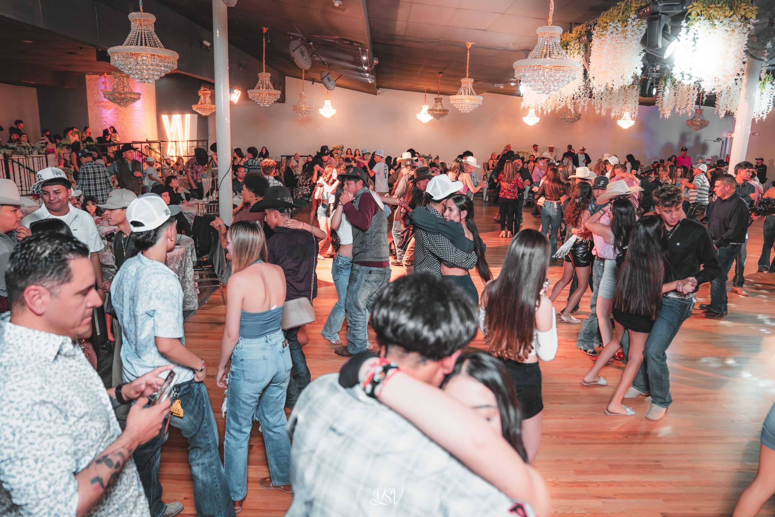 Couples dance together on a wooden floor at a social dance event with string lights overhead.