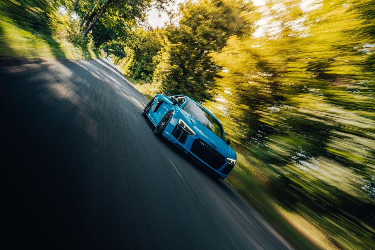 Blue sports car captured with motion blur on curved road.