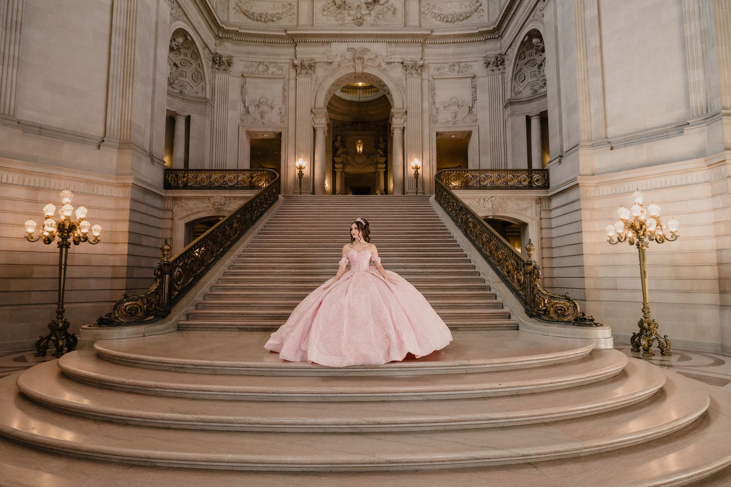 A grand marble staircase in an ornate building interior with elegant chandeliers and classical architectural details.