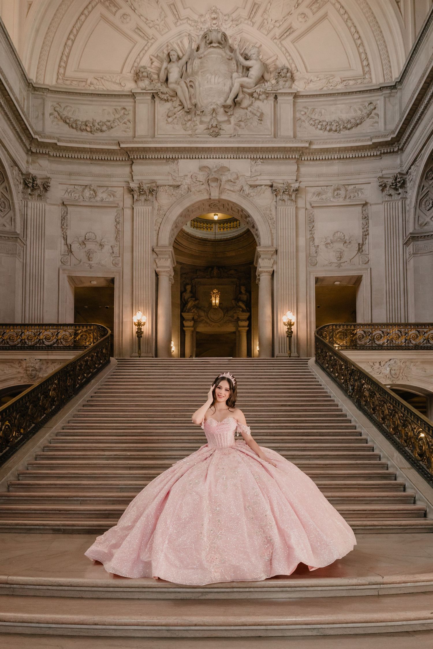 An elegant pink ballgown displayed in a luxurious marble staircase setting with ornate architectural details.