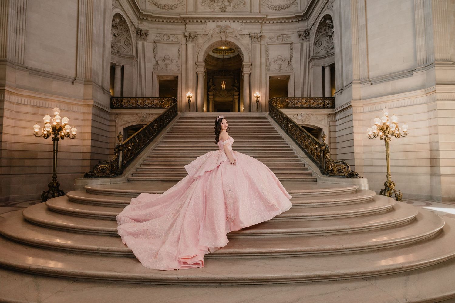 A person in a flowing pink ballgown poses elegantly on grand marble stairs in a luxurious palace setting.