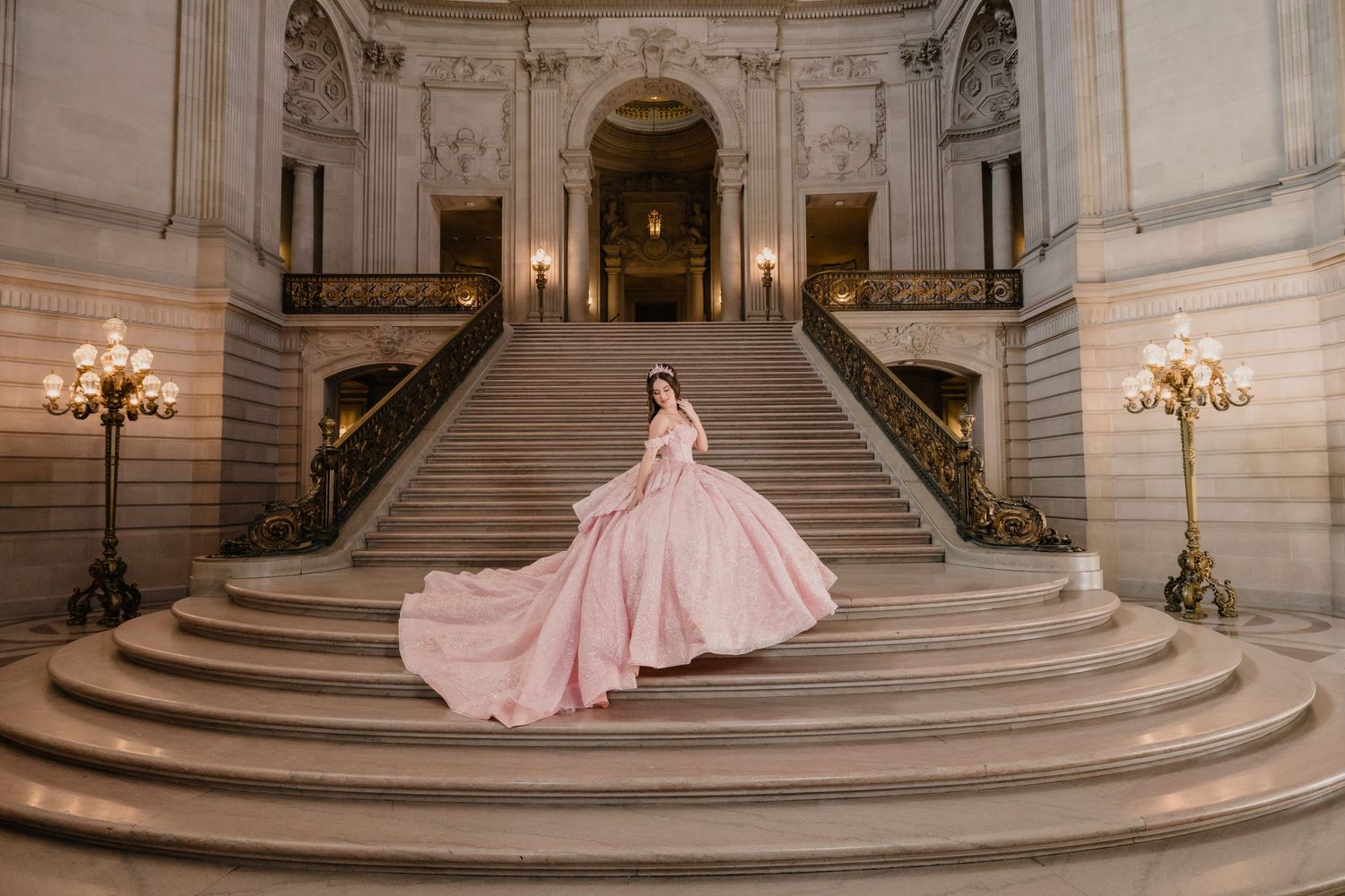 A flowing pink ballgown dress cascades down the grand marble staircase of an elegant historic building interior.