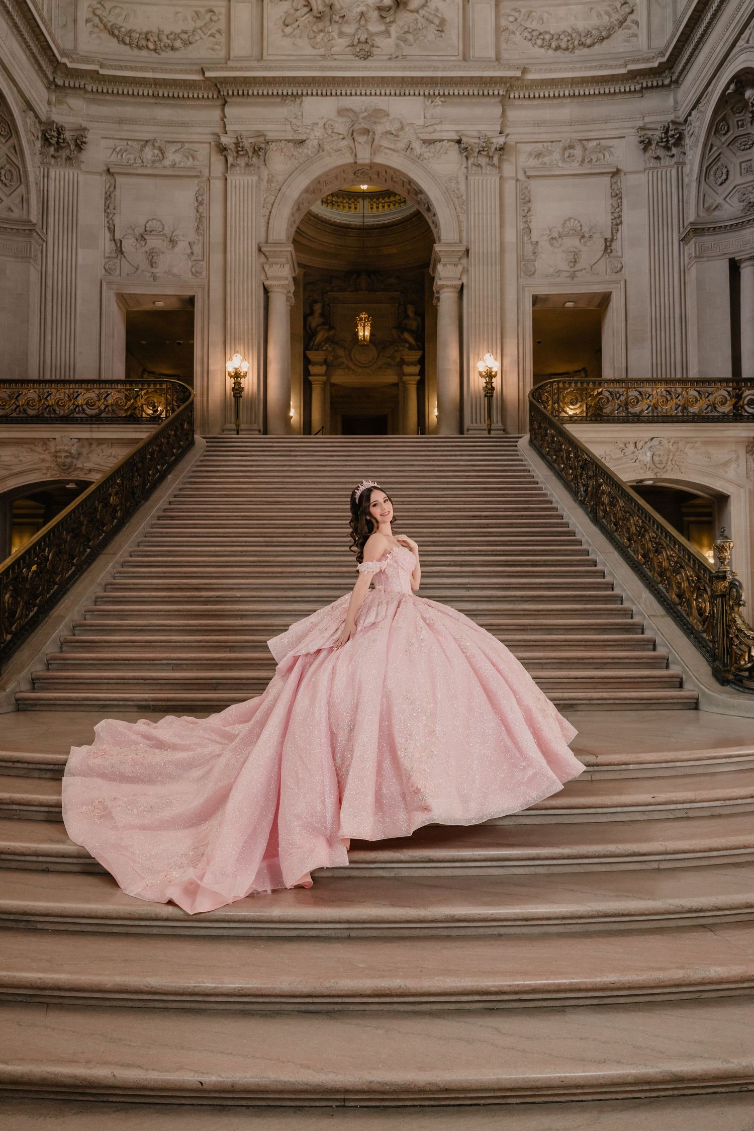 Dramatic shot of a pink ball gown against ornate white marble staircase and architectural details.