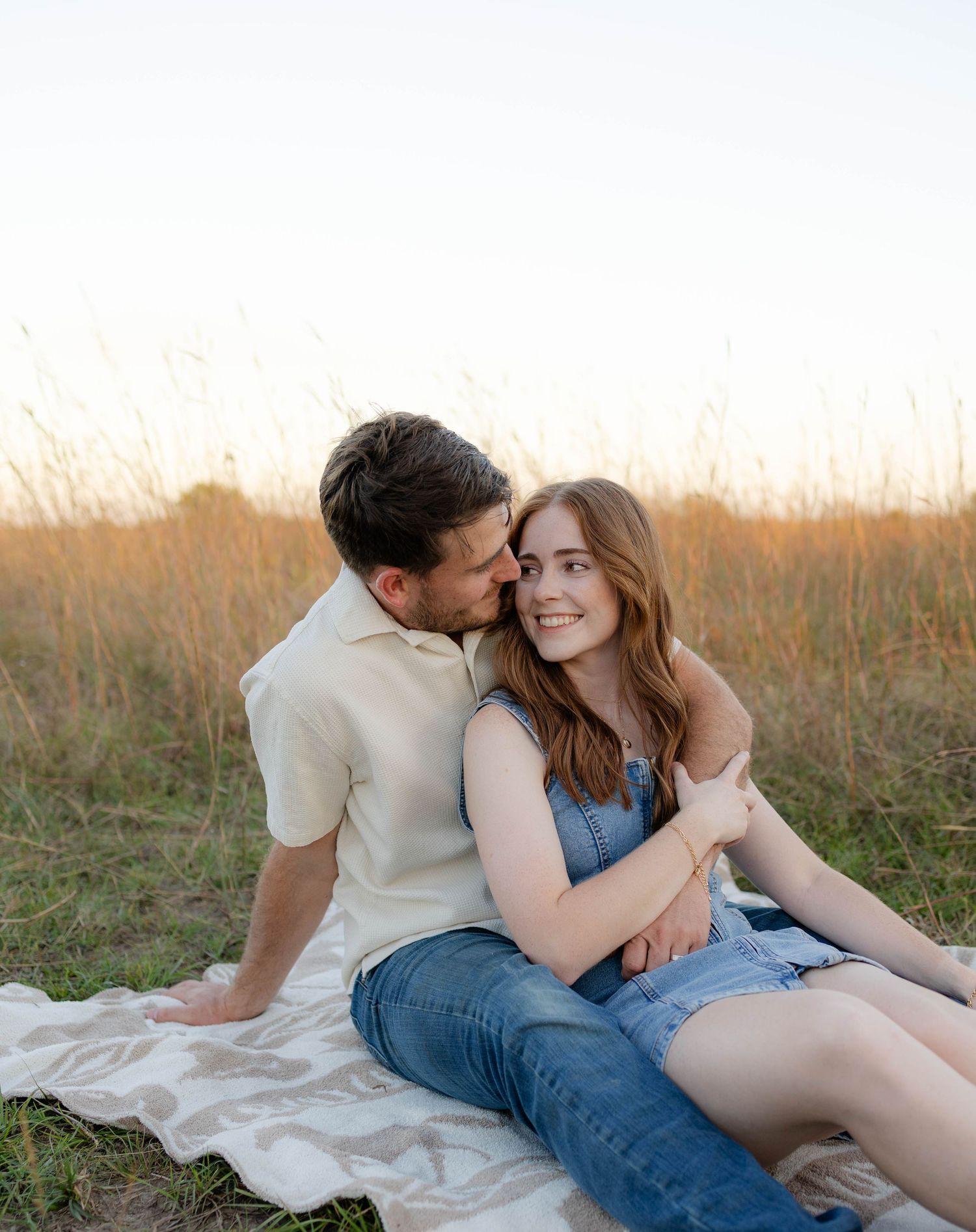 True West Photography - Couple sharing romantic moments on a blanket in a sunlit field.