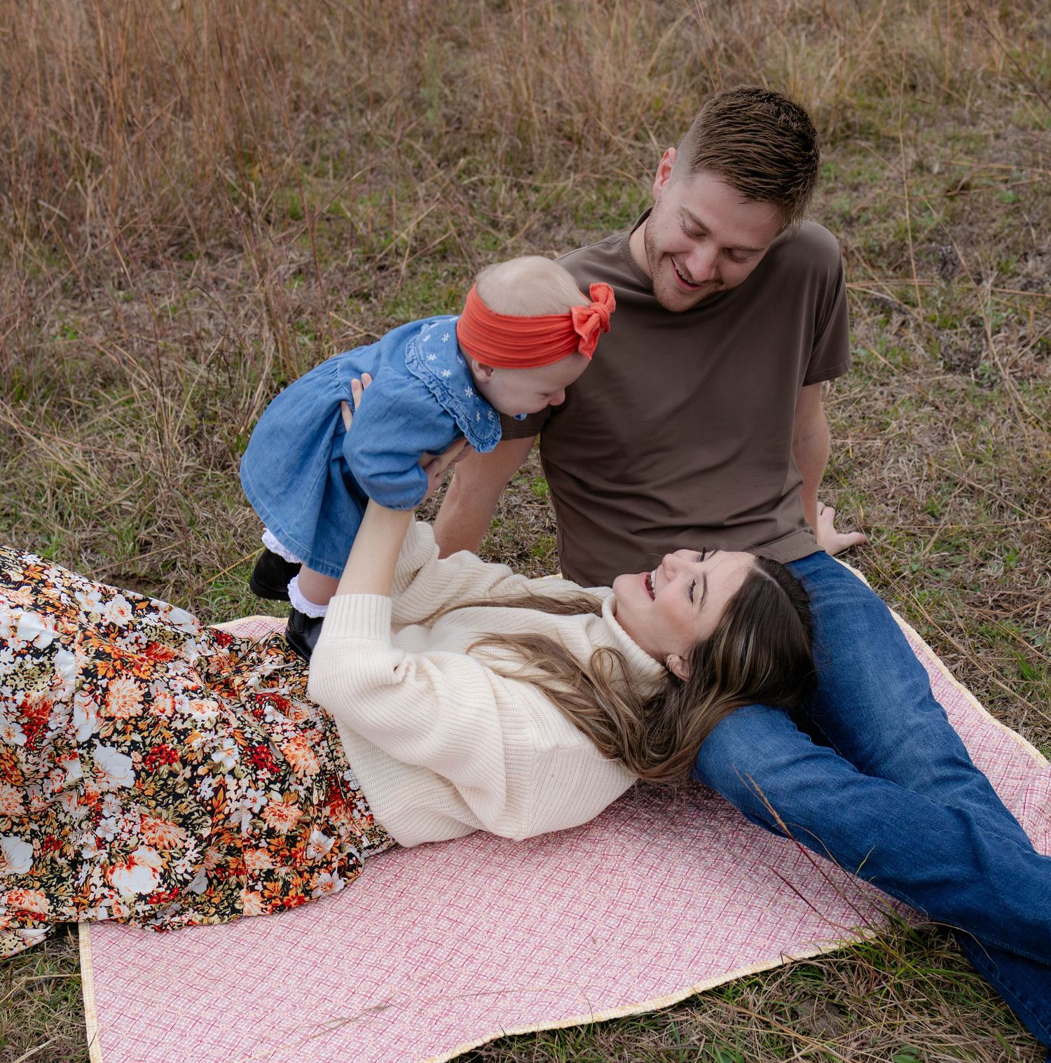 True West Photography - Playful couple lying on patterned blanket in grassy field.
