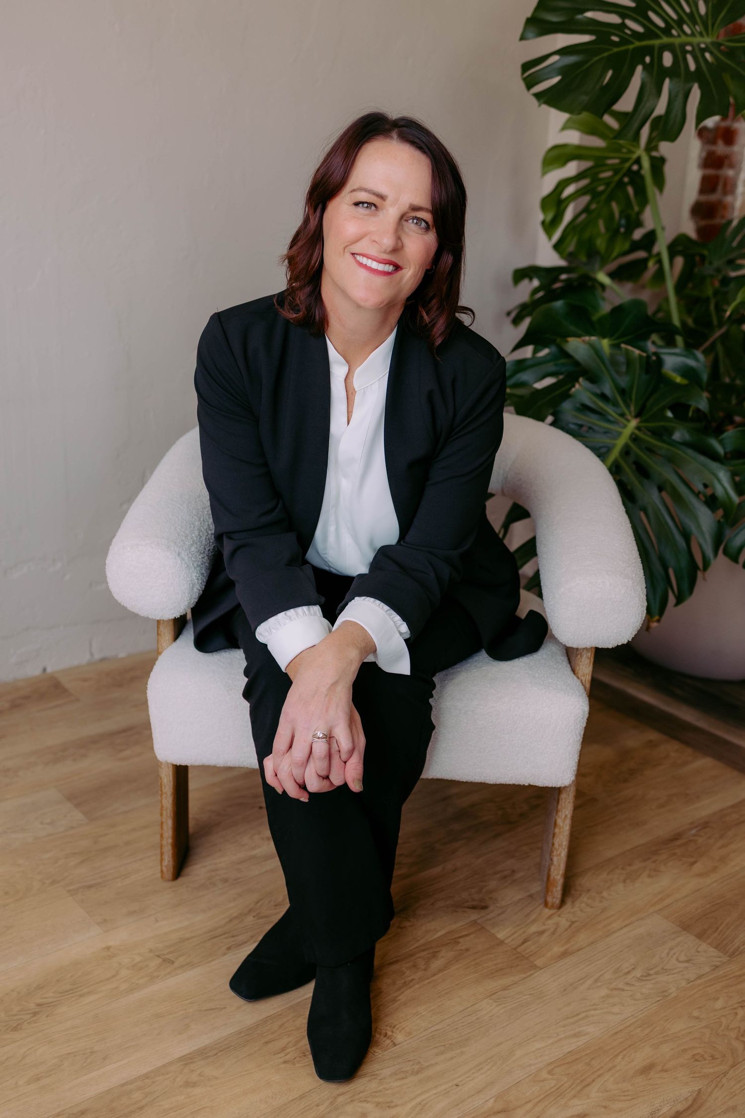 True West Photography - Business portrait of person in black suit sitting in white armchair with tropical plant.