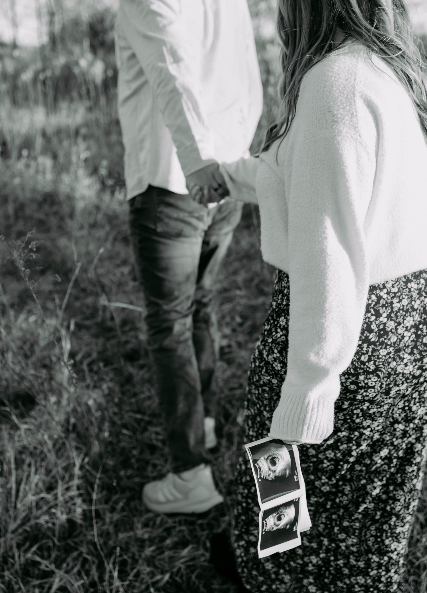 A black and white photo series showing close-up details of someone in white clothing walking through tall grass.