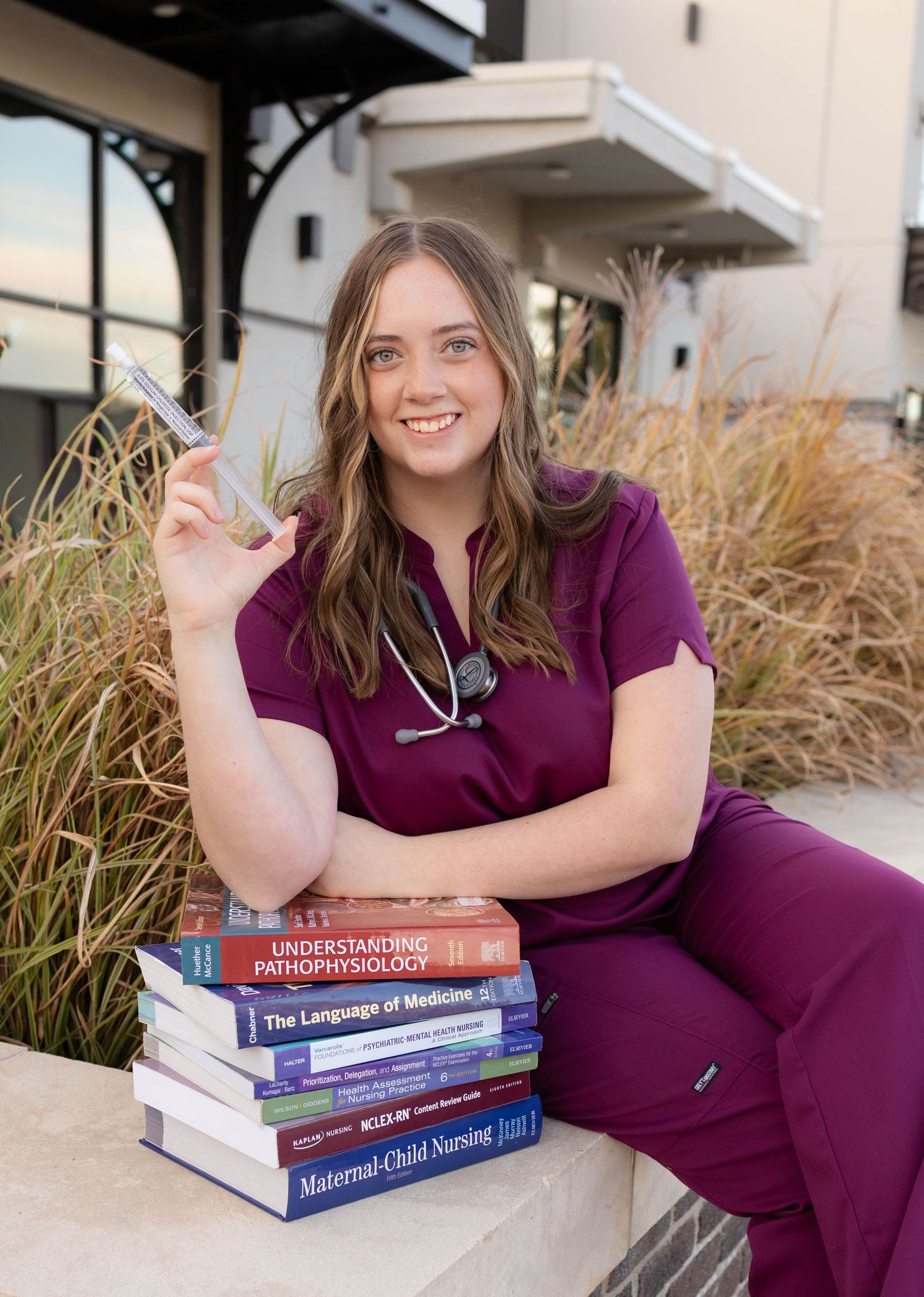 True West Photography - Person in scrubs posing with medical textbooks outside a building.