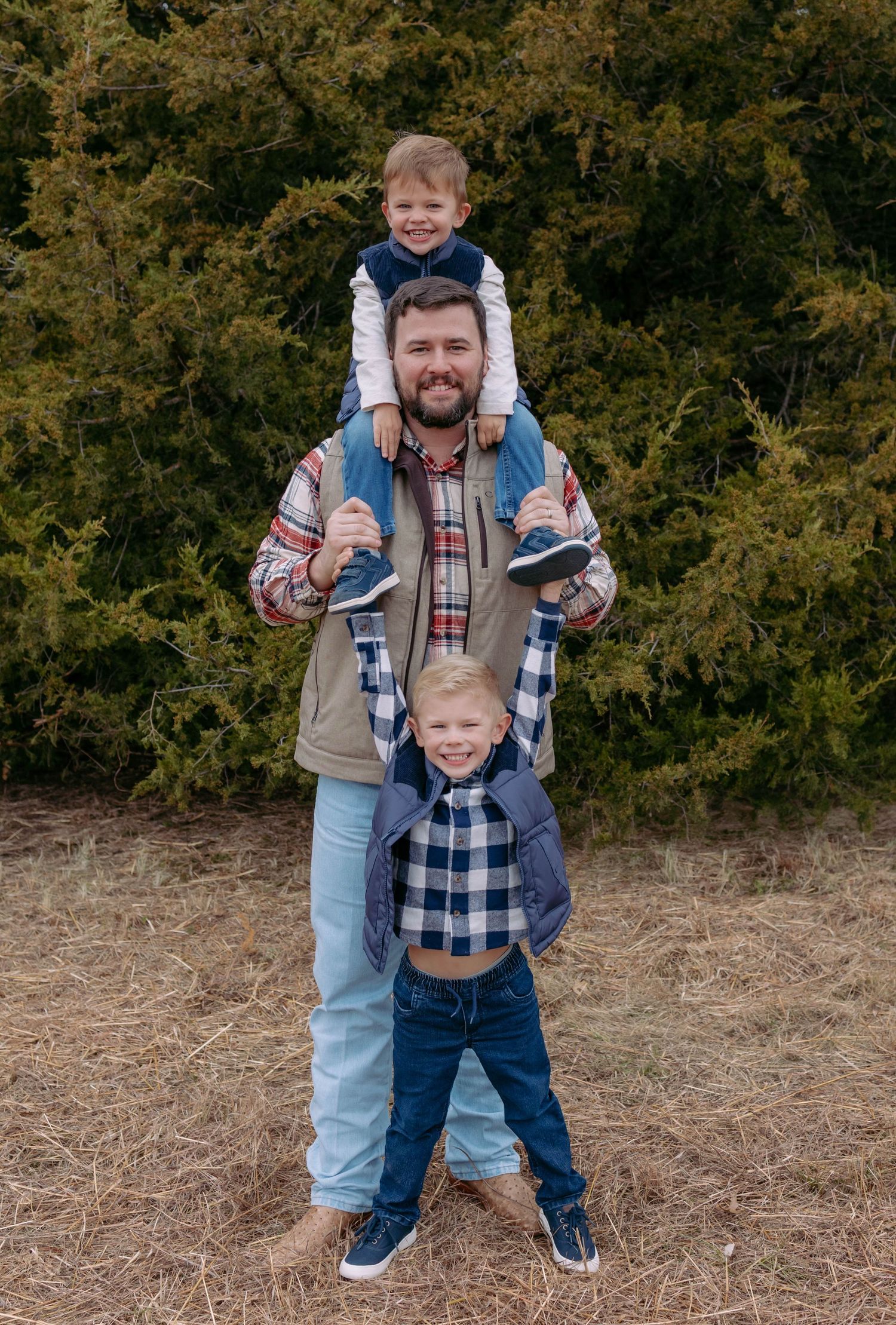A playful outdoor photoshoot showing family members in coordinating plaid shirts and jeans against a natural backdrop.