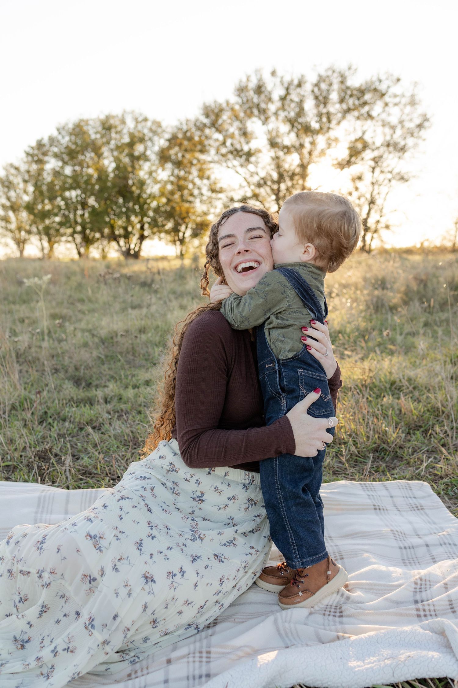 True West Photography - Two people share a joyful moment together on a blanket outdoors during golden hour.